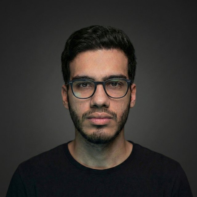 Abdallah Elraai, photographed straight-on against a dark grey background.